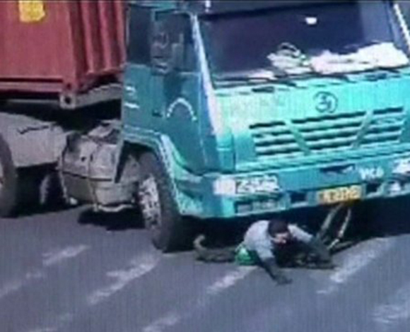 بالفيديو: سائق دراجة ينجو من الموت بعد مرور شاحنة فوقه