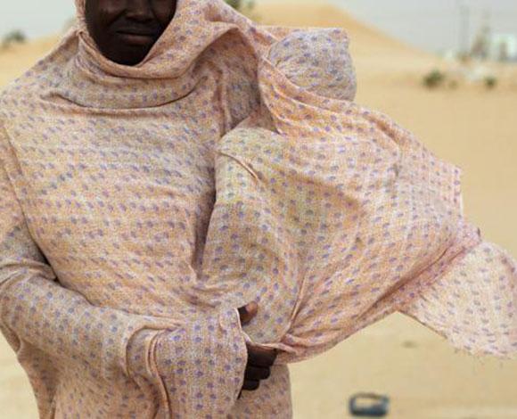 امرأة موريتانية تحمي طفلها من الرياح الرملية القوية بوشاحها الرديء